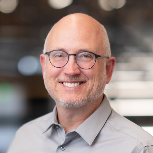 Eric Madsen, smiling man in glasses and gray shirt