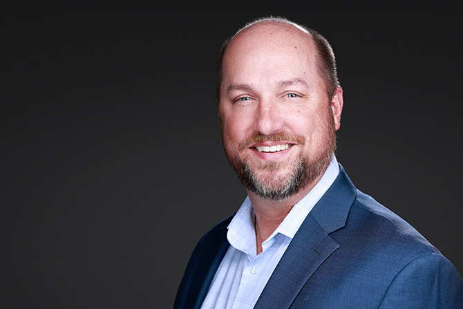 Bruce T. Fallon, smiling in suit and plaid shirt