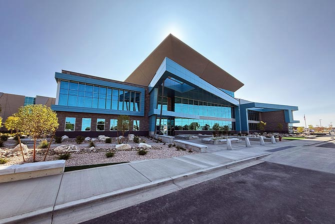 Modern building with angular architecture and large glass windows, set against a clear blue sky. Landscaping includes small trees and rocks, conveying a sleek, professional ambiance.