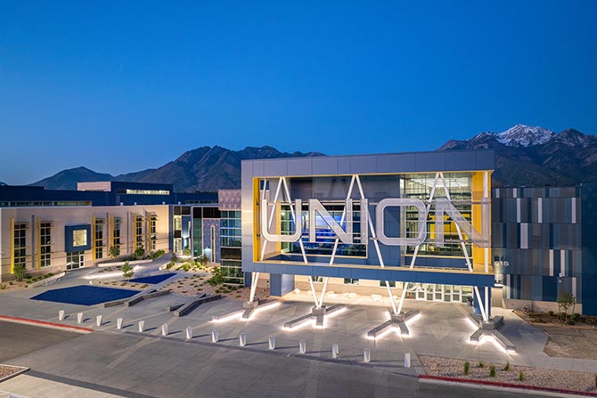 Modern building with "UNION" sign, large glass windows, and geometric design, set against a dusk sky and mountainous backdrop. Calm and illuminated.