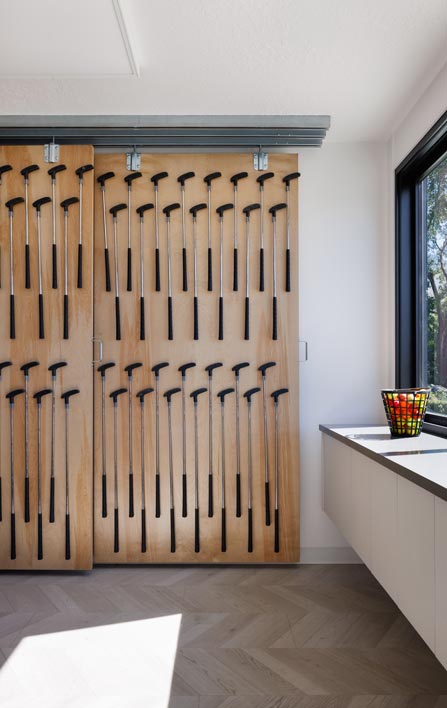 Sliding wooden doors with evenly spaced black canes hanging, create a geometric pattern. Sunlit room with parquet flooring, counter with colorful bowl, and large window.